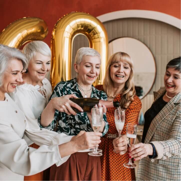 Older women pouring champagne into glasses in front of balloons