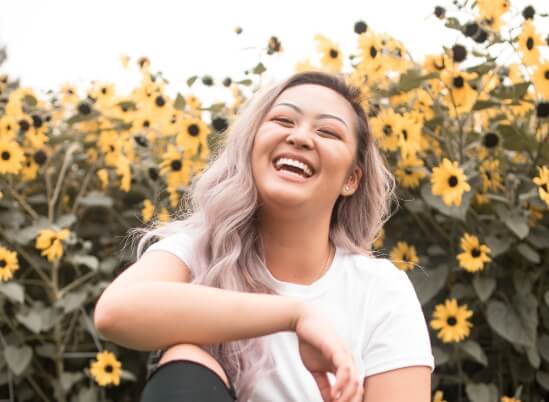 Young woman sitting in a sunflower field smiling